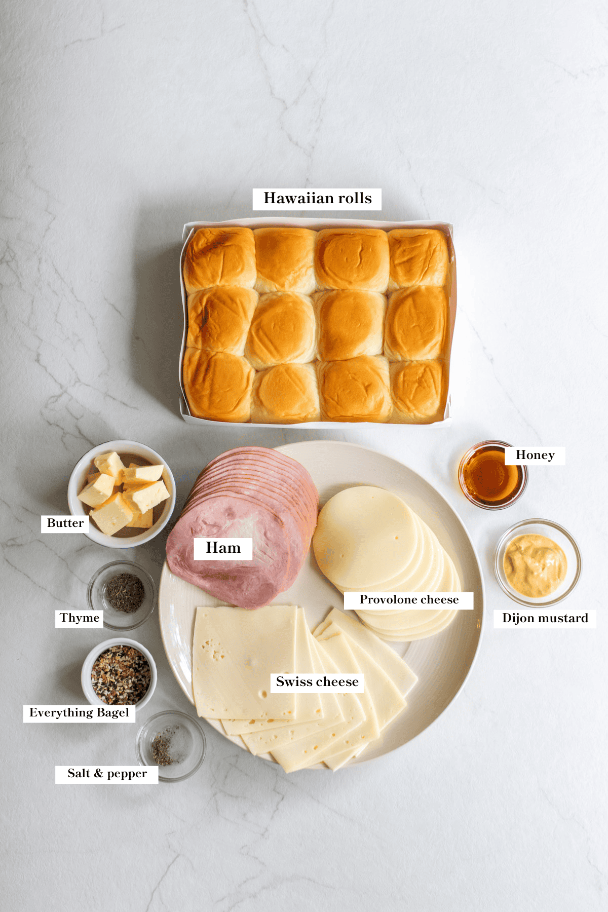 Hawaiian rolls, a plate of ham and cheese, and other ingredients on a countertop.