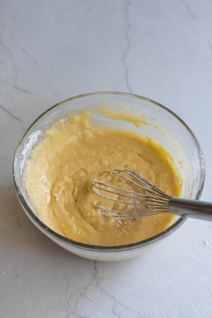 Cake batter mixed together in a glass bowl with a whisk.