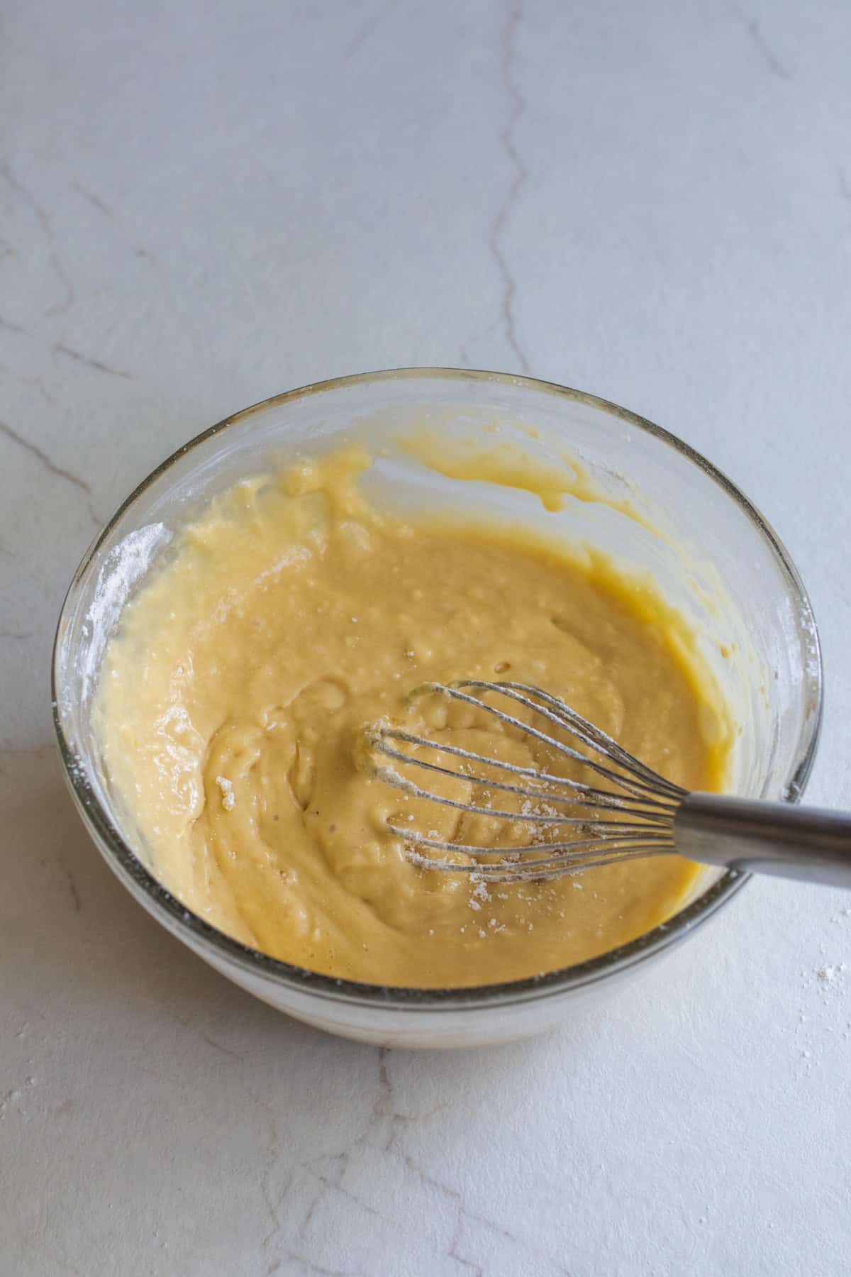 Cake batter mixed together in a glass bowl with a whisk.