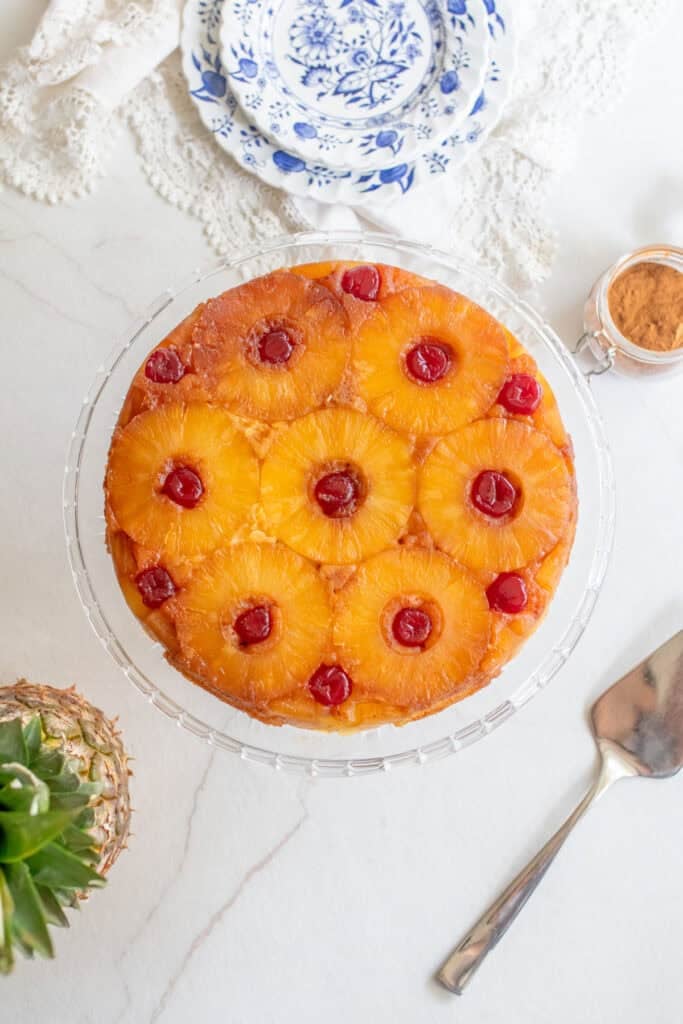 Overhead photo of a pineapple upside down cake on a glass cake plate. 