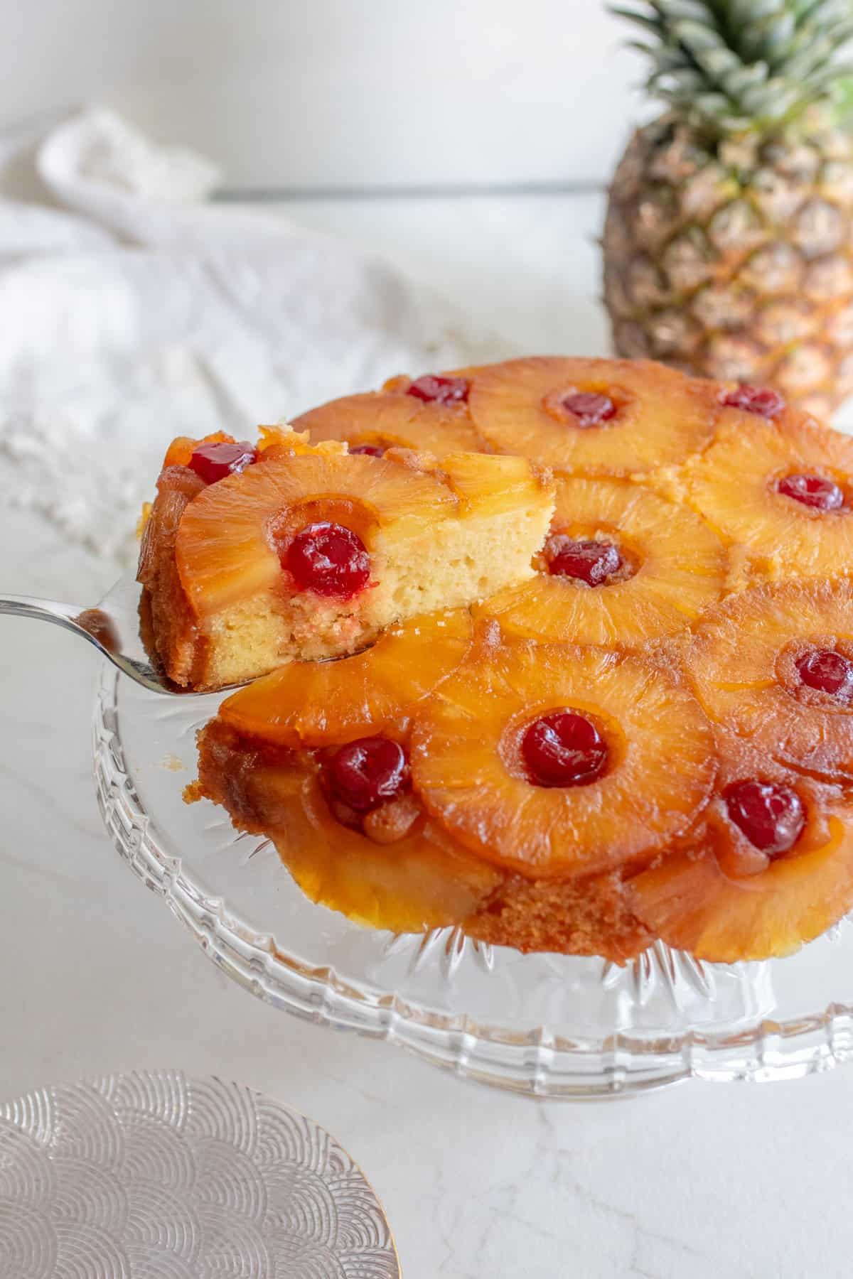Slice of pineapple upside down cake on a glass cake stand.