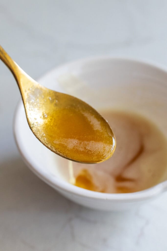 A spoon full of brown butter with a bowl of more browned butter in the background.