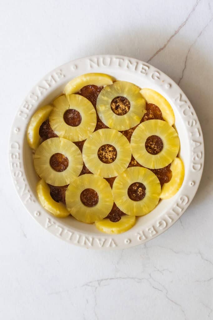 Canned pineapple slices placed on top of browned butter, cinnamon and brown sugar in a pie plate. 