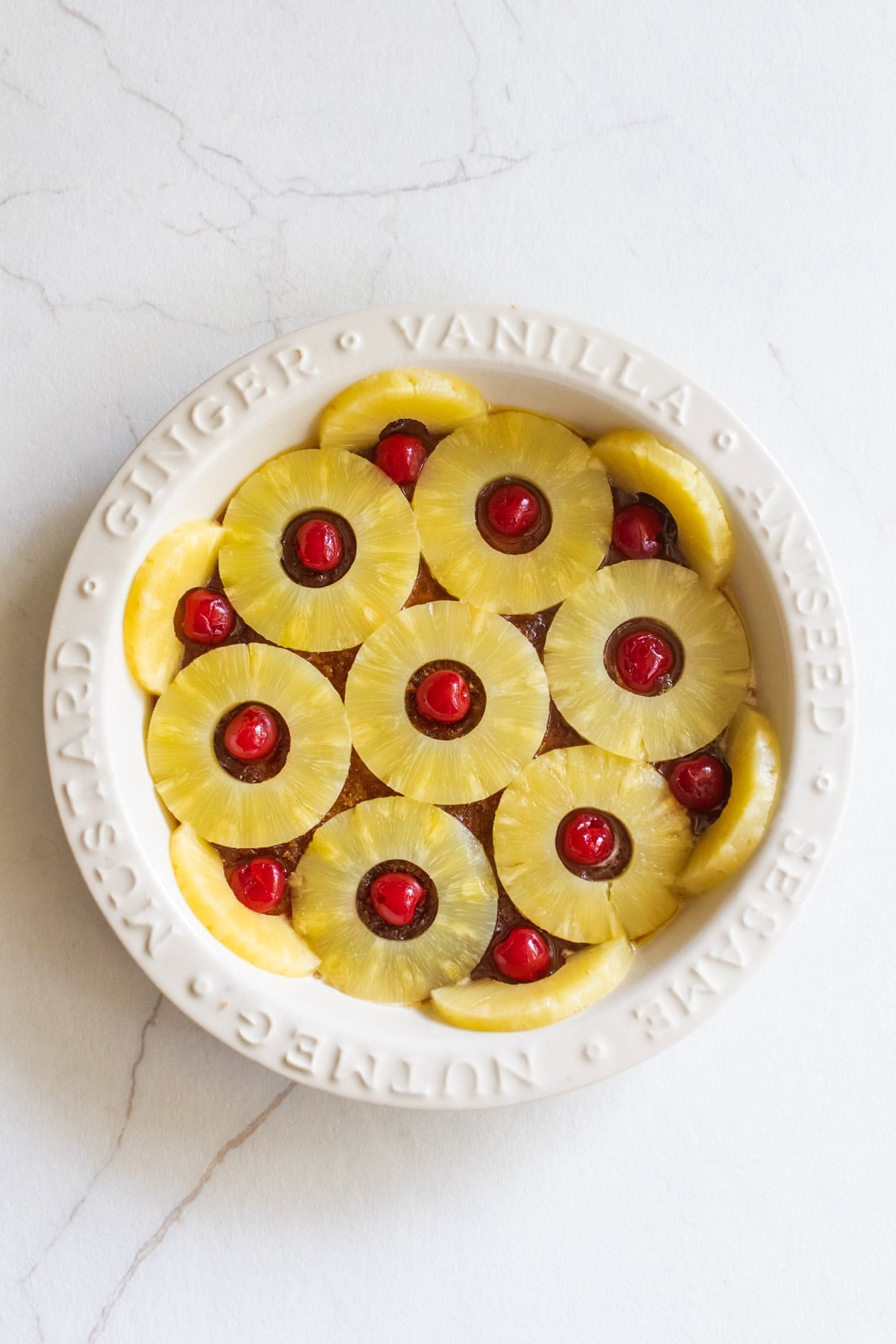 Maraschino cherries in the center of sliced pineapple rings in a pie pan.