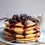five pancakes covered in blueberry sauce sitting on a blue plate.