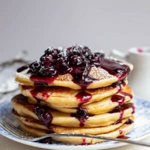 five pancakes covered in blueberry sauce sitting on a blue plate.