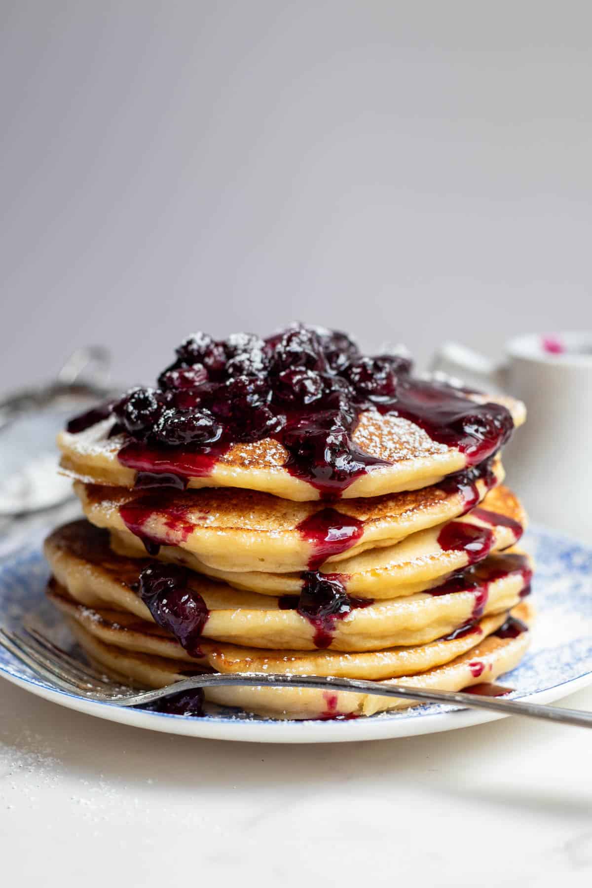 Five pancakes covered in blueberry sauce sitting on a blue plate.