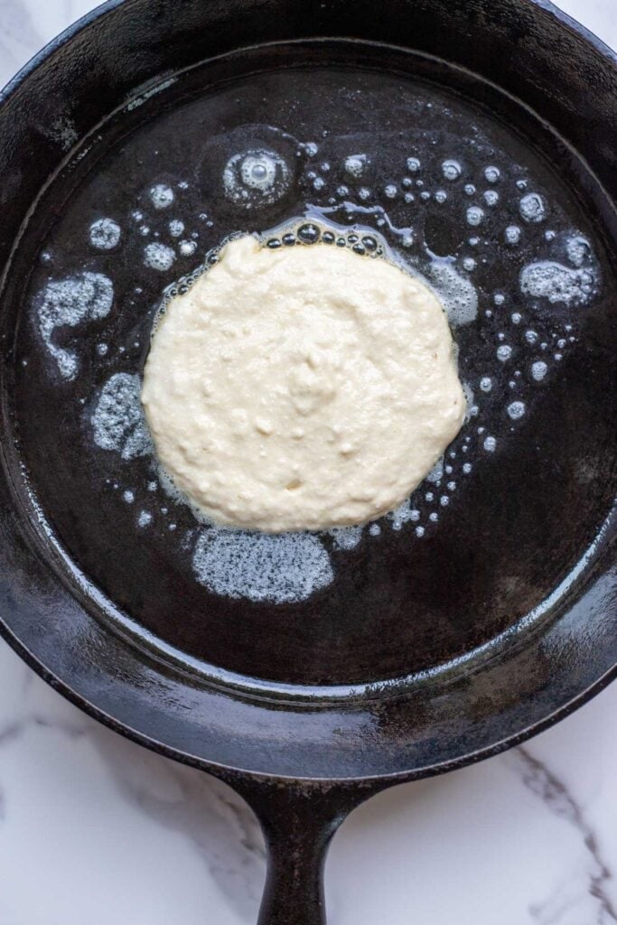 A pancake cooking in a skillet with butter.