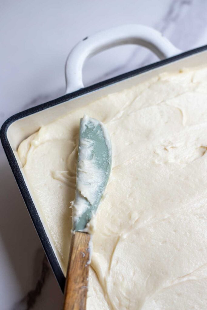 A knife applying cream cheese frosting to a cake.