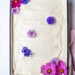a cake iced with white cream cheese frosting and decorated with pink and purple flowers.