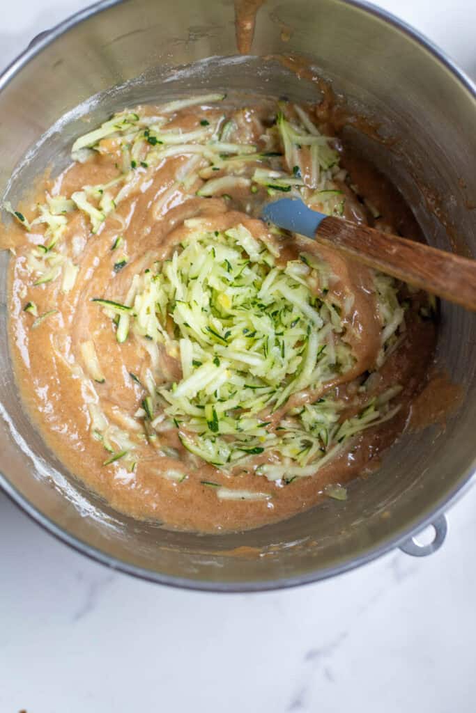 Zucchini added into a cake batter in the mixing bowl.
