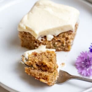 A bite sized piece of cake sitting on a white plate with a fork underneath.