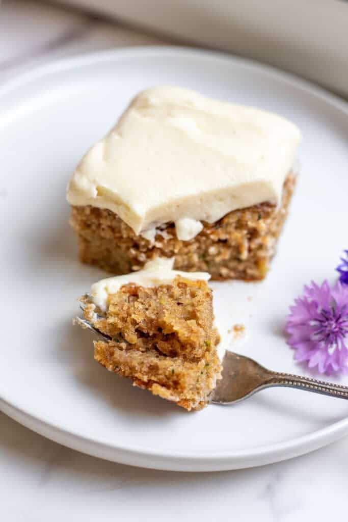 A bite sized piece of cake sitting on a white plate with a fork underneath.