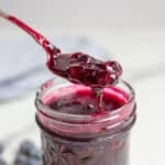 a spoon covered in blueberry sauce right above a pint jar of blueberry sauce.