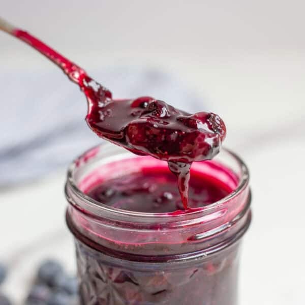 a spoon covered in blueberry sauce right above a pint jar of blueberry sauce.