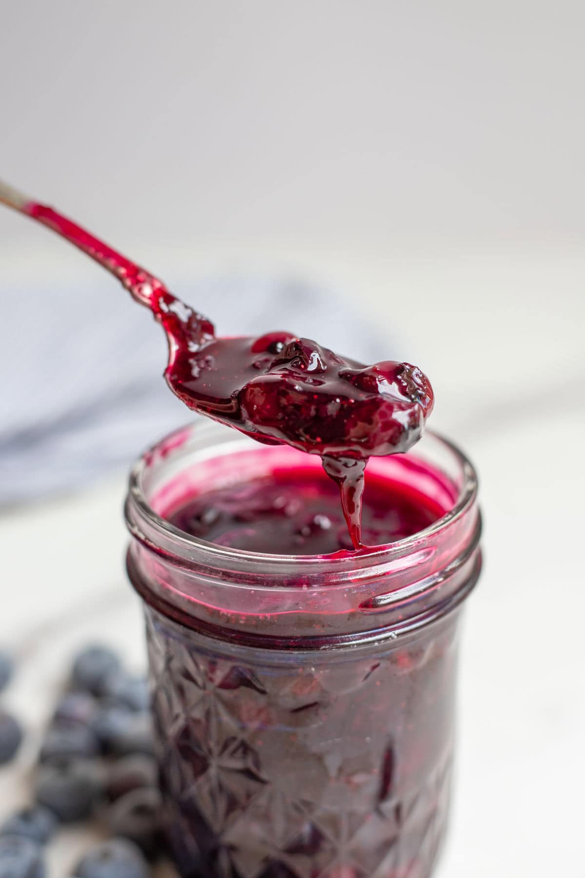 A spoon covered in blueberry sauce over a pint jar of blueberry sauce.