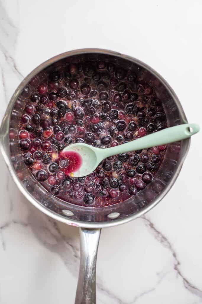 Blueberries simmering in a pot with a ladle dipped into the sauce.