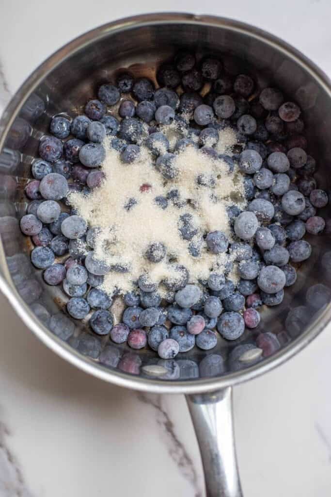 Blueberries and sugar in a simmering pot on the stove. 