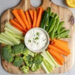 a cutting board with fresh vegetables and ranch dip.