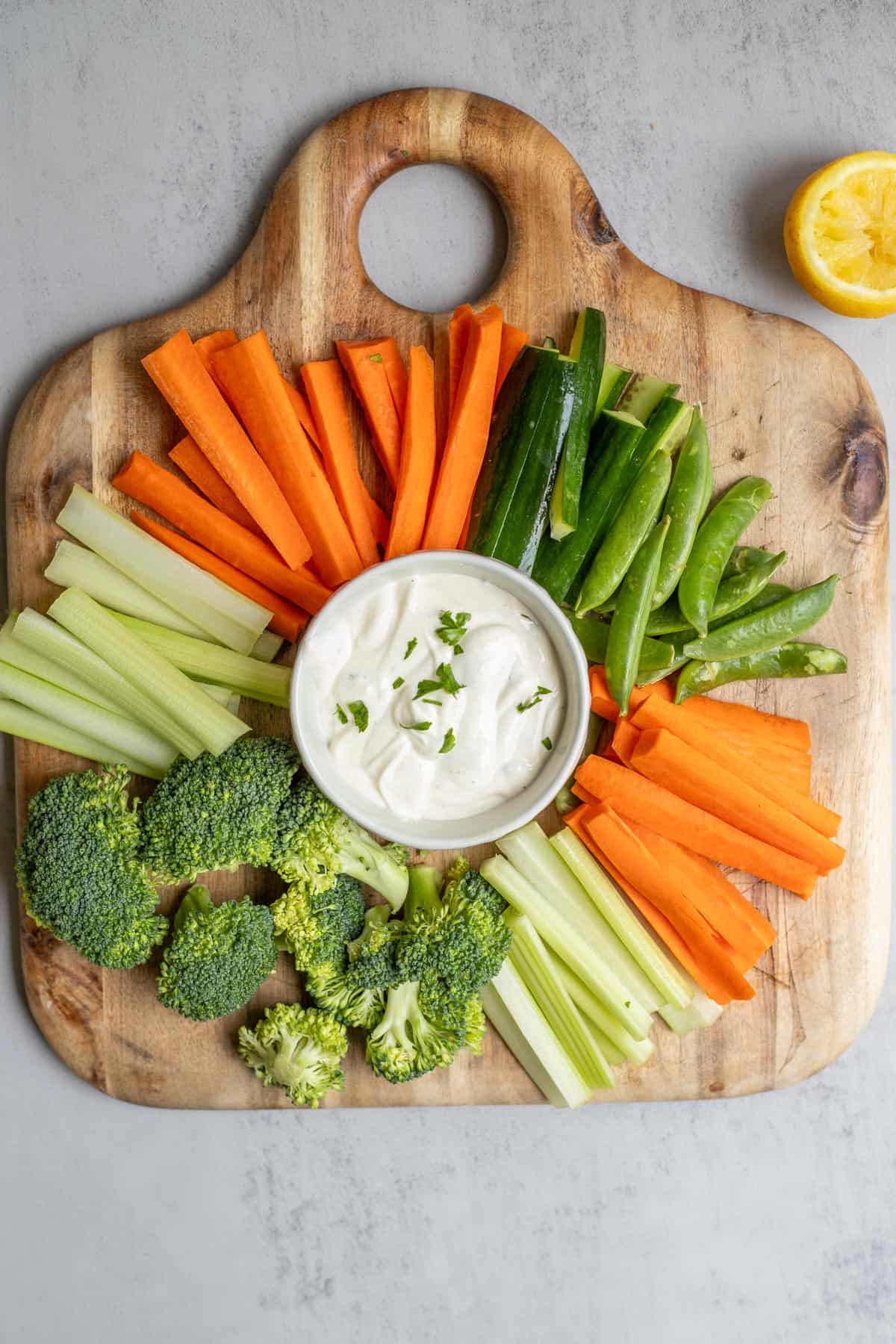 A cutting board with fresh vegetables and ranch dip.
