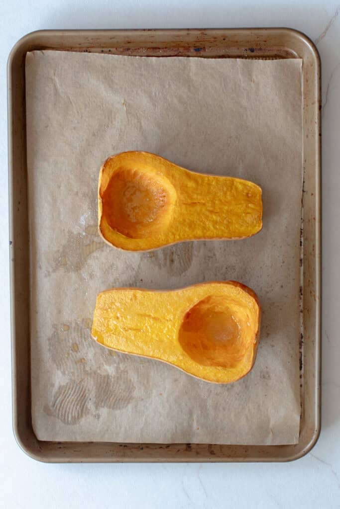 Roasted butternut squash sliced in half on a baking sheet.