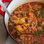 A dutch oven full of cabbage roll soup with a ladle food of soup coming out of the dutch oven.