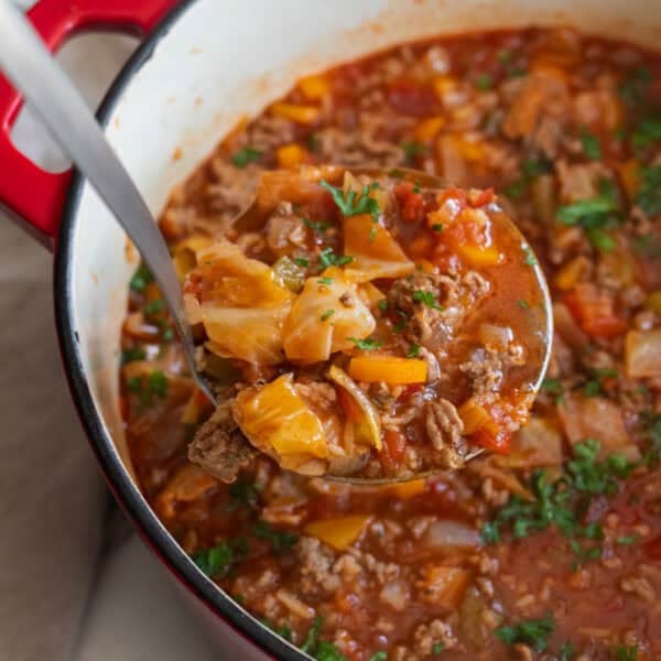 A dutch oven full of cabbage roll soup with a ladle food of soup coming out of the dutch oven.