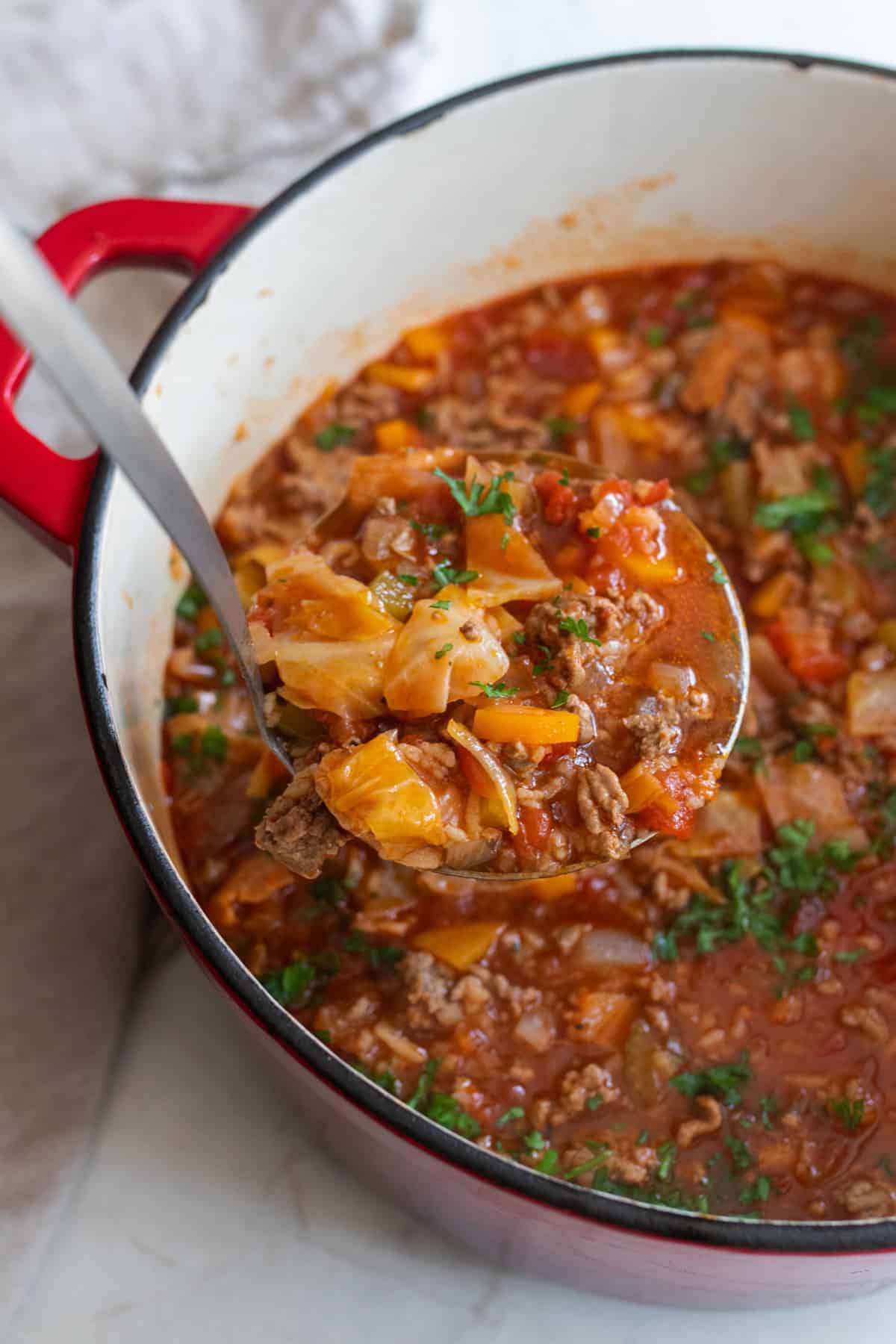 A ladle of cabbage roll soup lifting out of a Dutch oven.