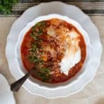 Cabbage soup served with sour cream and fresh herbs in a white bowl on a white plate.