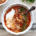 Cabbage roll soup in a white bowl on a stripped tablecloth.