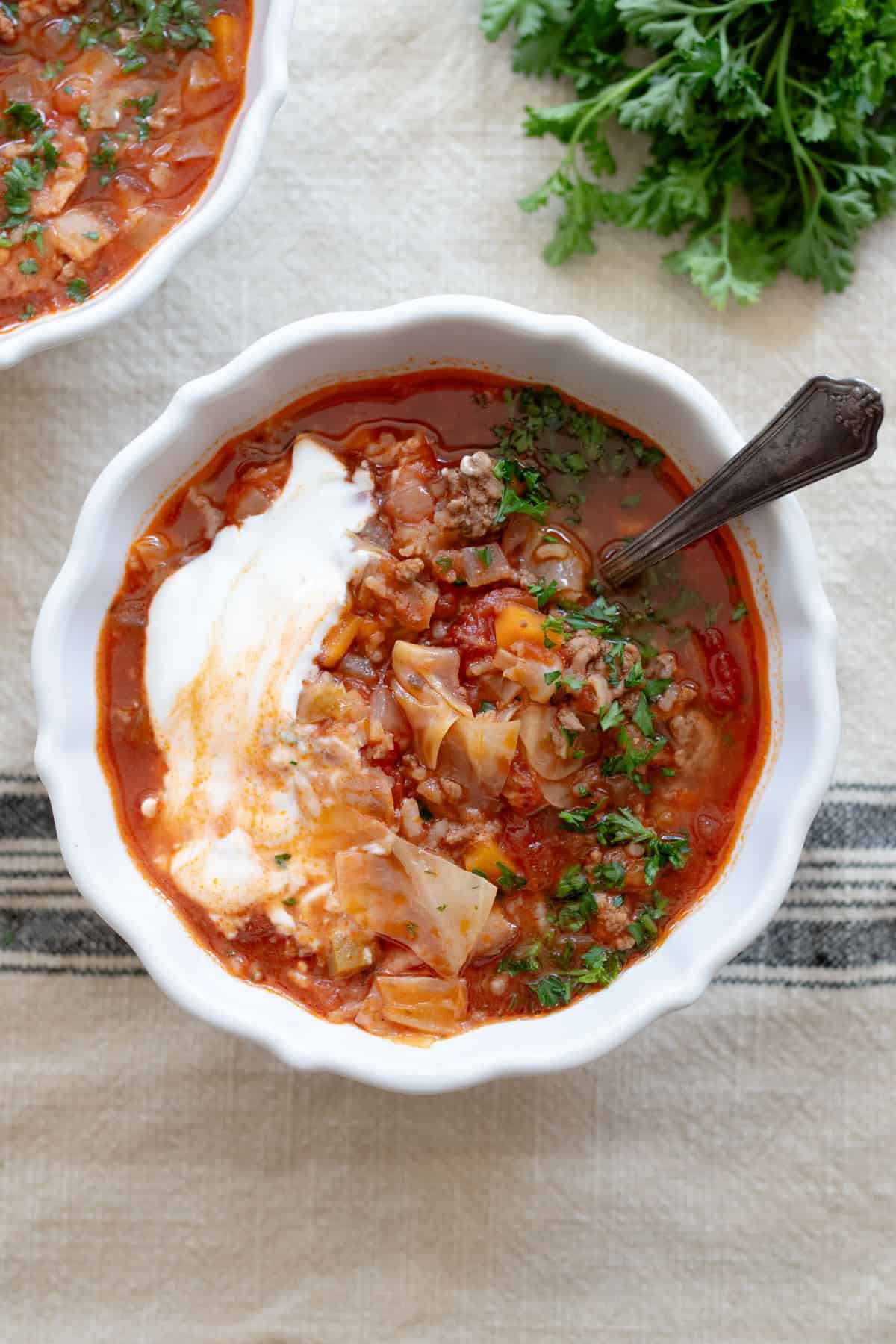 Cabbage roll soup in a white bowl on a stripped tablecloth.