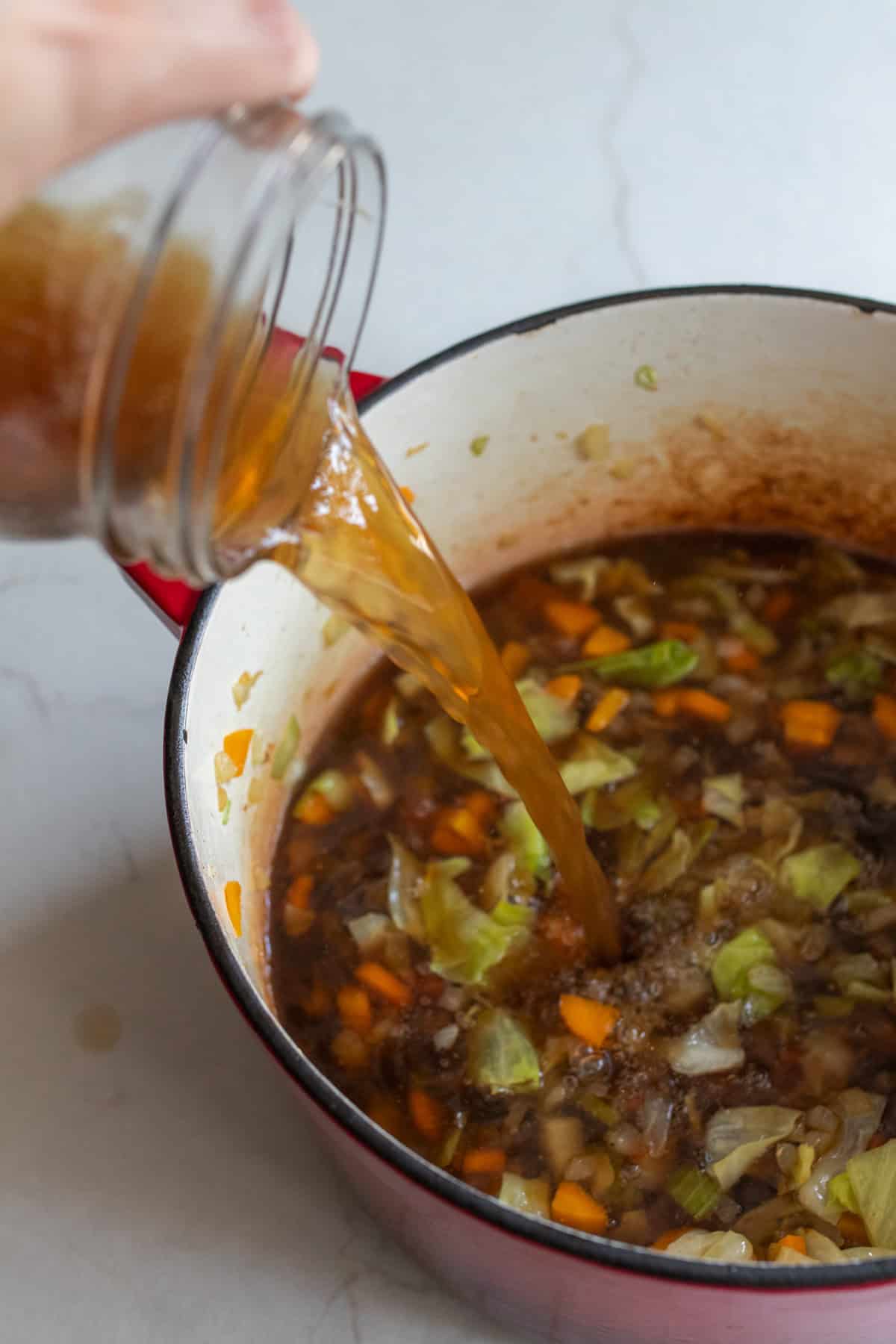 Adding broth to veggies to a Dutch oven with other veggies.