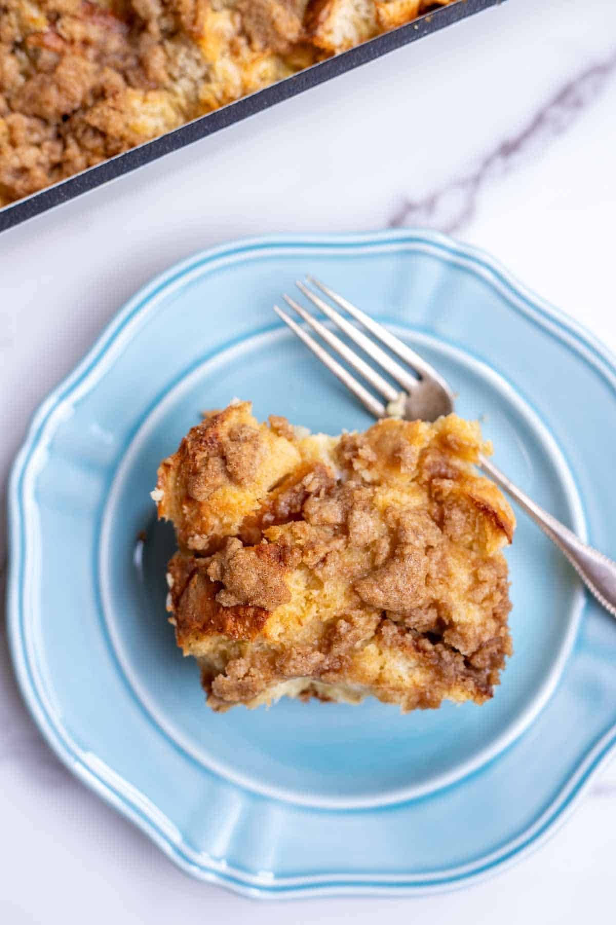 A slice of French toast casserole on a blue plate with a fork.