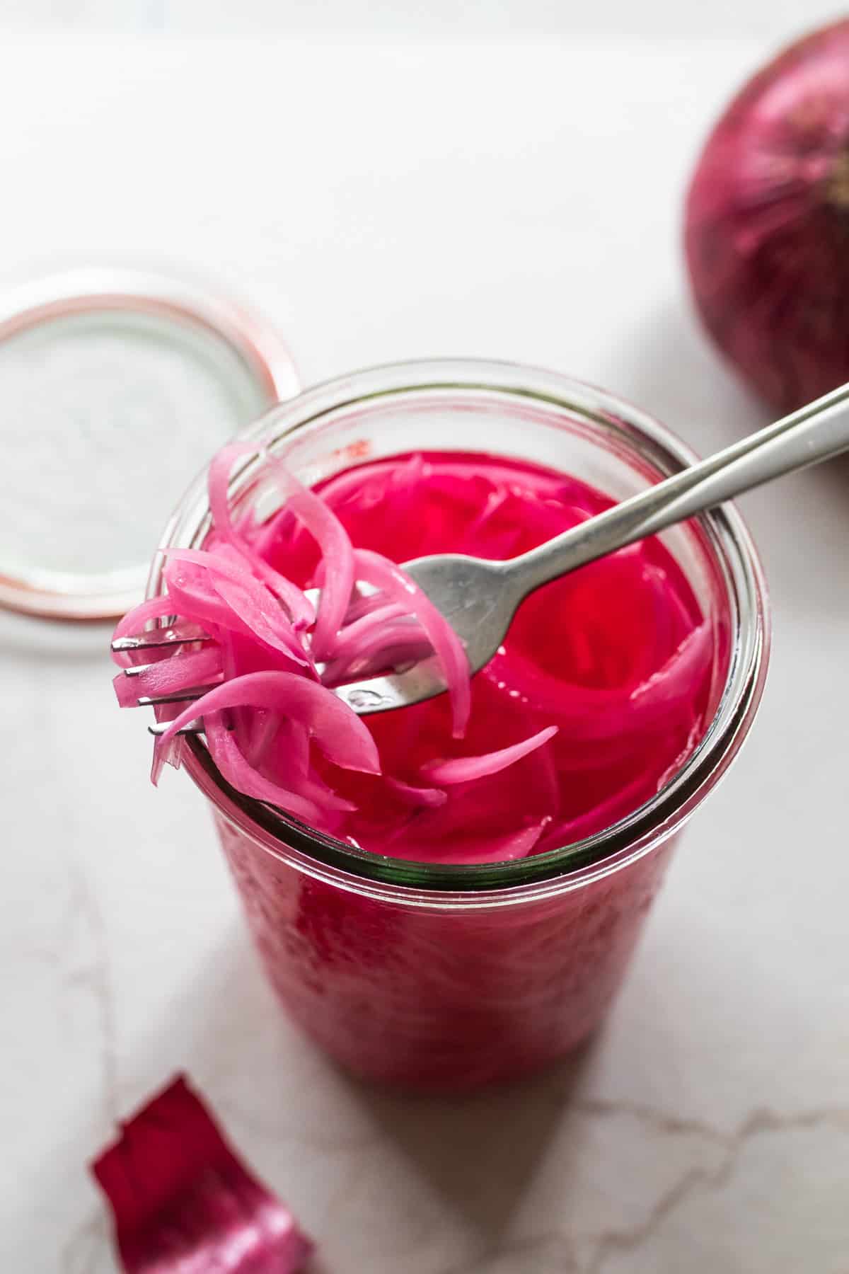 Jar of pickled red onions with a fork full of pickled onions.