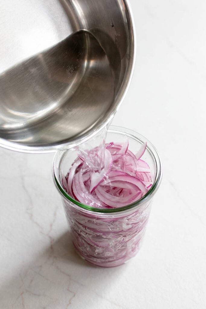 Pouring brine into jar with sliced red onion.