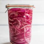 Pickled red onion in a weck jar with a lid on a white countertop.