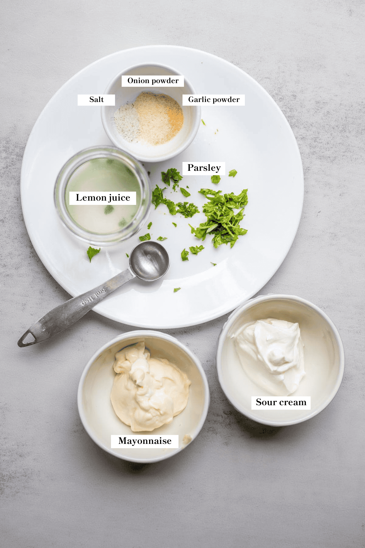 Mayonnaise, sour cream, parsley, lemon juice, and spices on the counter.