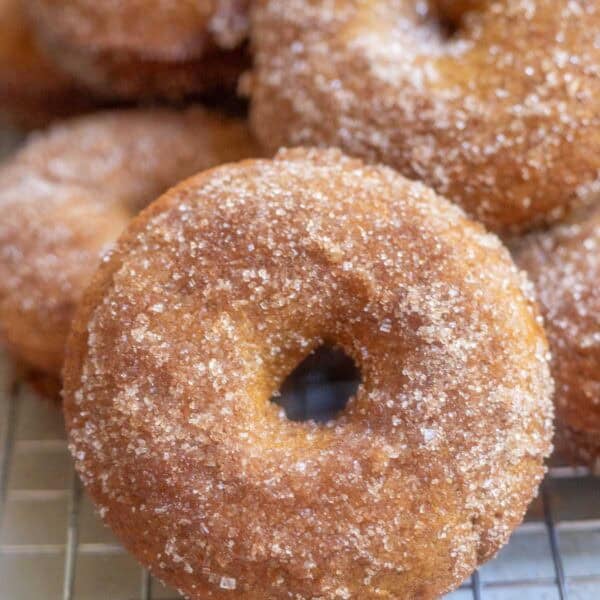 apple cider donuts stacked on top of each other on a wire cooling rack.