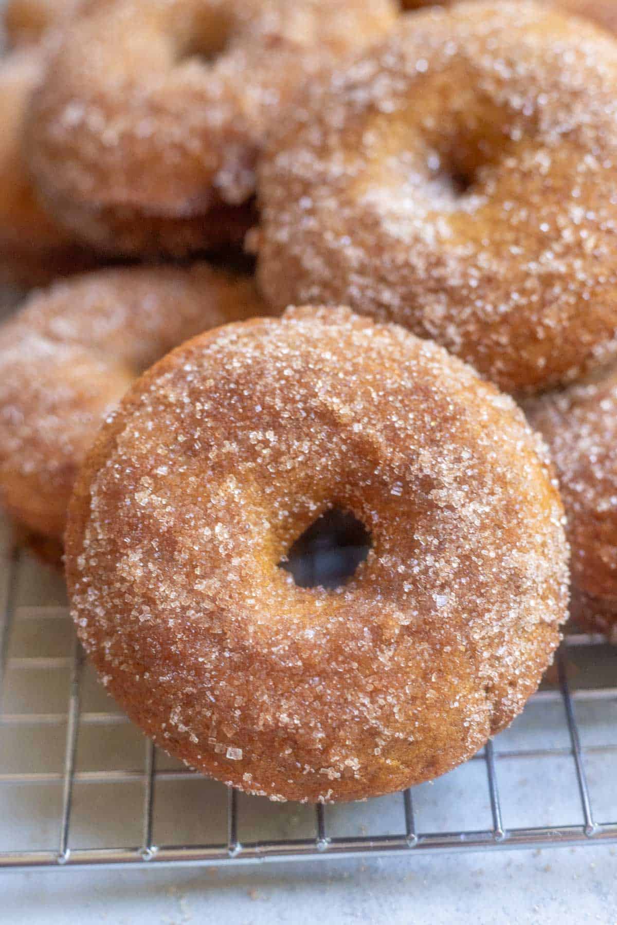 Apple cider donuts stacked on top of each other on a wire cooling rack.