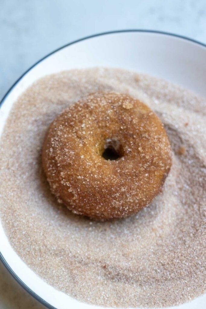 A donut being coated in brown sugar and cinnamon after it was dipped in melted butter.
