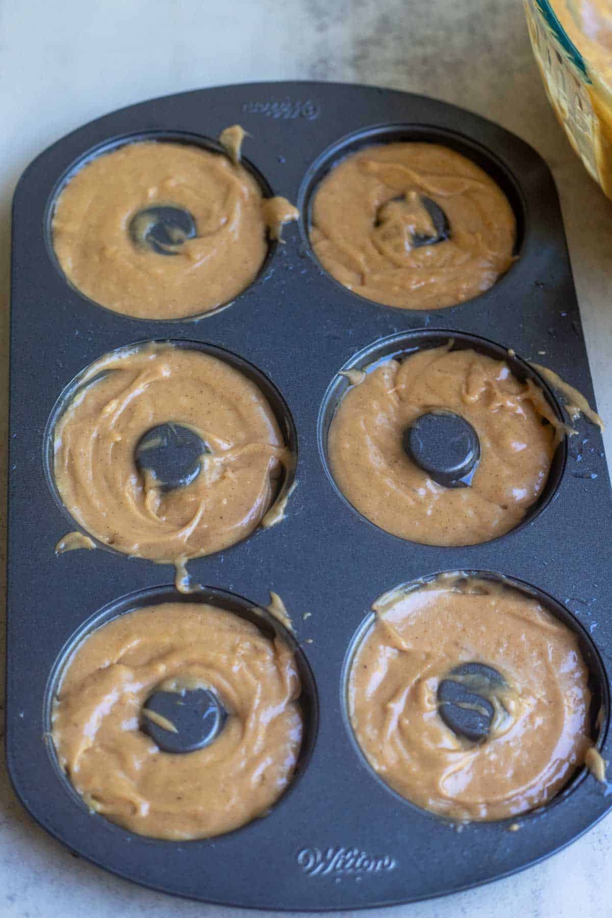 donut batter piped into a greased donut pan.