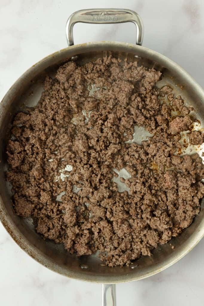 Ground beef browning in a stainless steel pan.