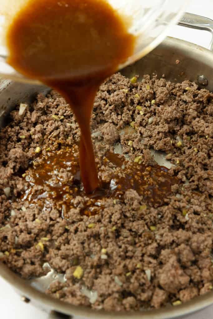 Pouring sauce into seasoned ground beef.