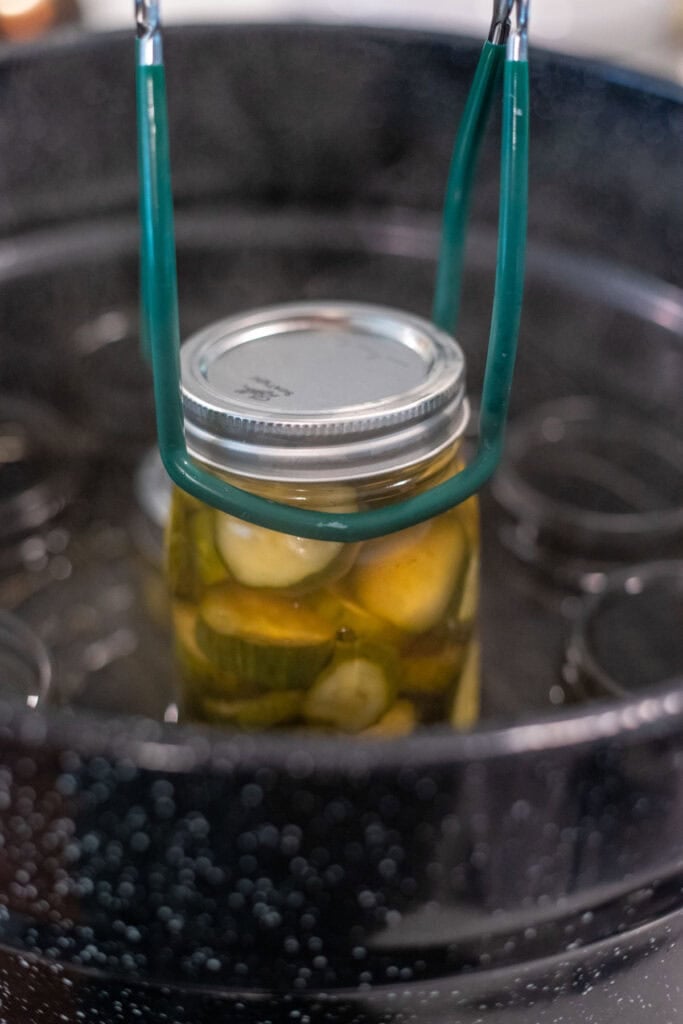 A jar of pickles being placed into a large water bath canner.