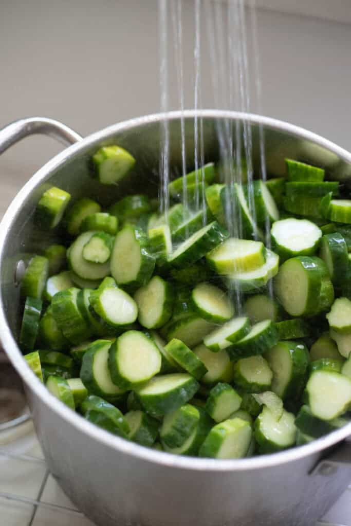 Sliced cucumbers in a colander being rinsed off with water.