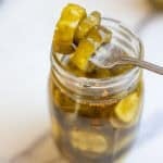 a fork stuck through three pickles on top of the glass jar.