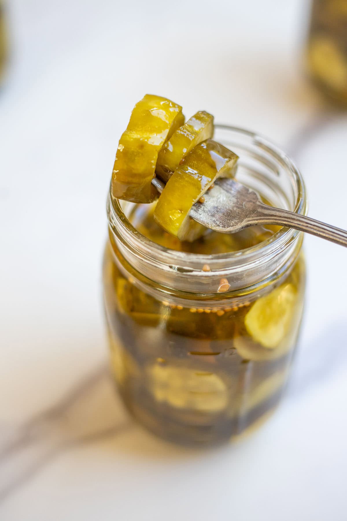 A fork stuck through three pickles on top of the glass jar.