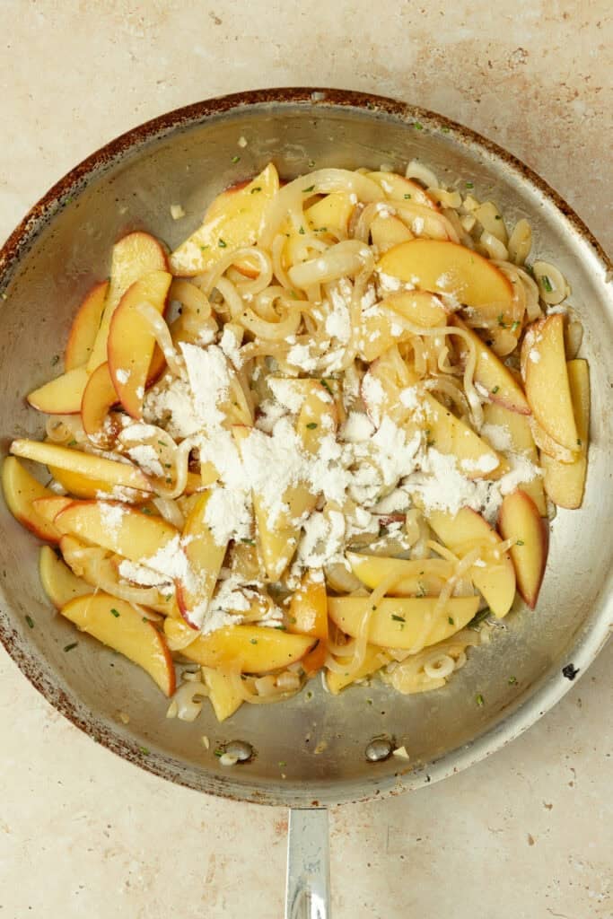 Adding flour into apples and onions in a skillet.