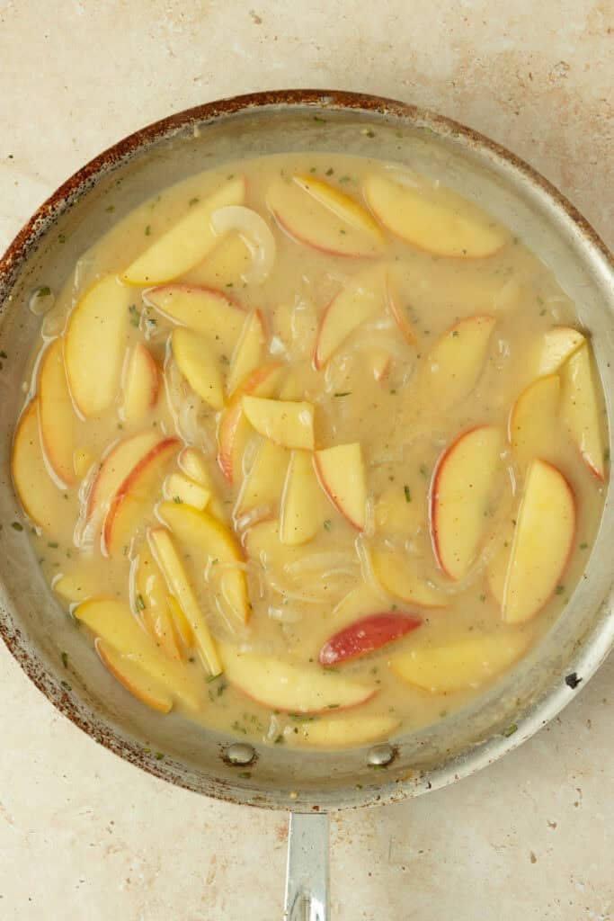 Broth added to a skillet with apples and onions.