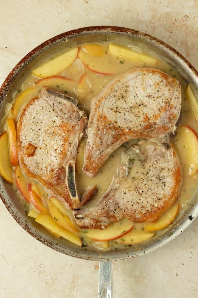 Pork chops added to a skillet with apples and onions.